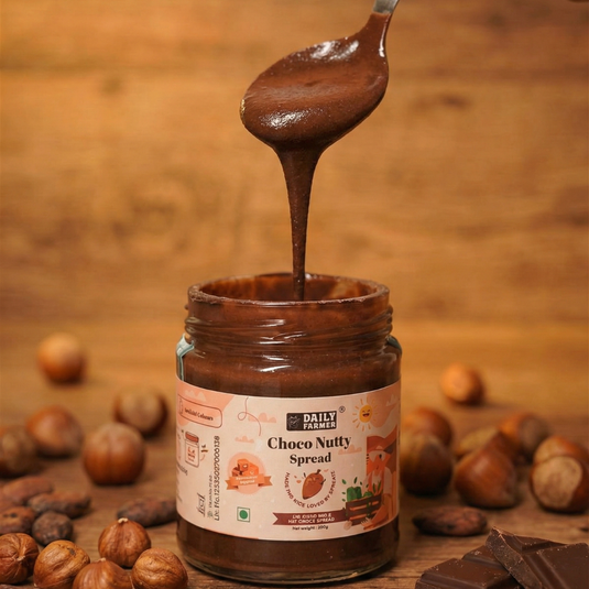 Jar of Choco Nutty Spread with a spoonful being poured, surrounded by nuts and chocolate pieces on a wooden background.