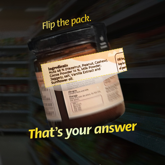 Jar of chocolate powder with a label showing ingredients, set against a blurred store shelf background.